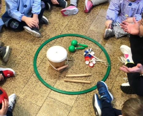 Bambini in cerchi attorno ad un cerchio che contiene un tamburello con le bacchette e i sonagli